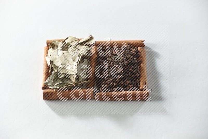 مربعان من أعواد القرفة ممتلئان بالقرنفل وأوراق الغار علي خلفية بيضاء