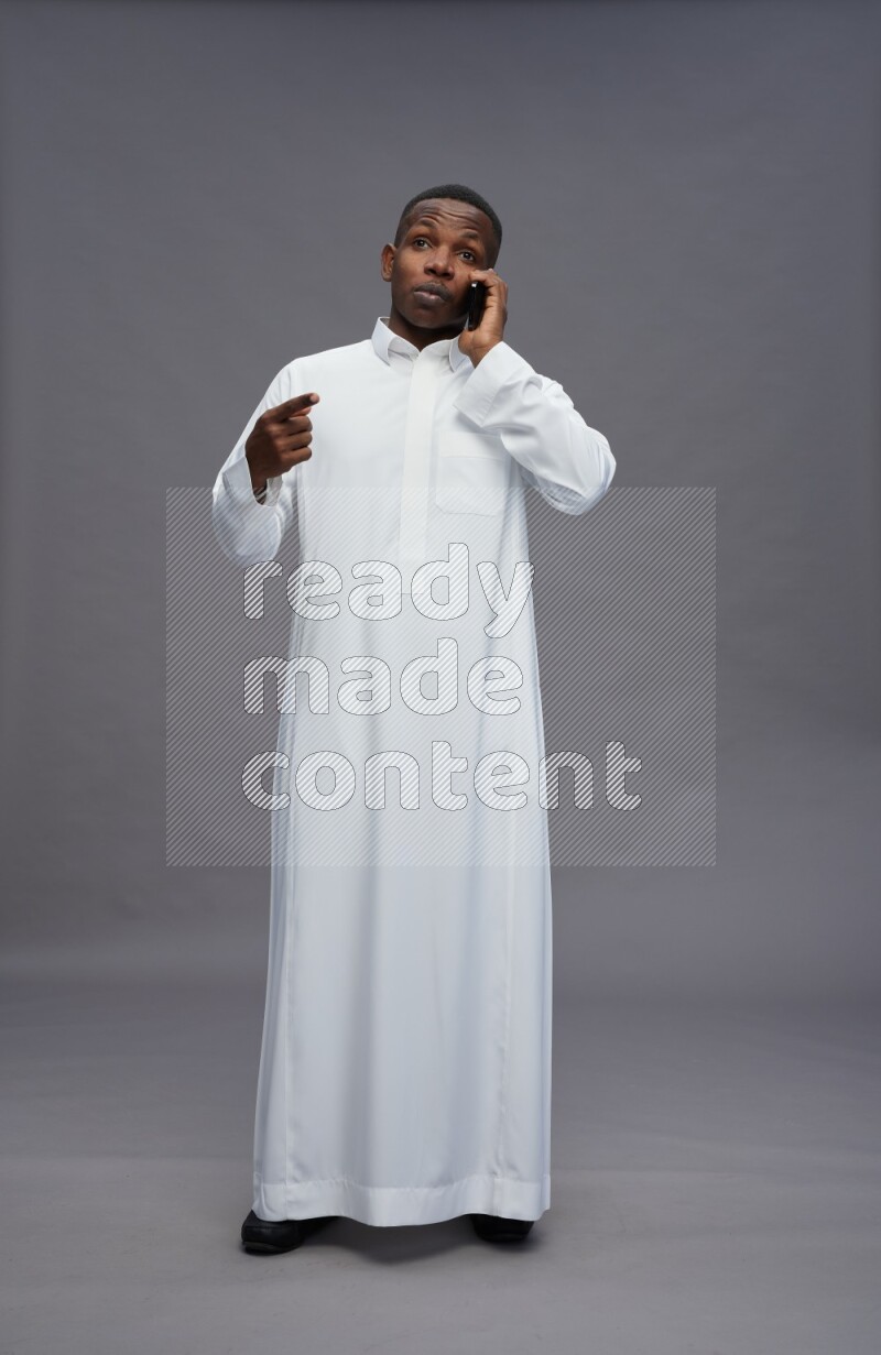 Saudi man wearing thob standing talking on phone on gray background