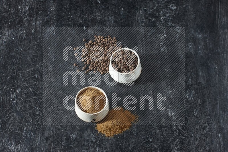 وعاءان بيج، أحدهما ممتلئ ببودرة بهار الفلفل الحلو والآخر بالحبوب وكلاهما متناثران على خلفية سوداء