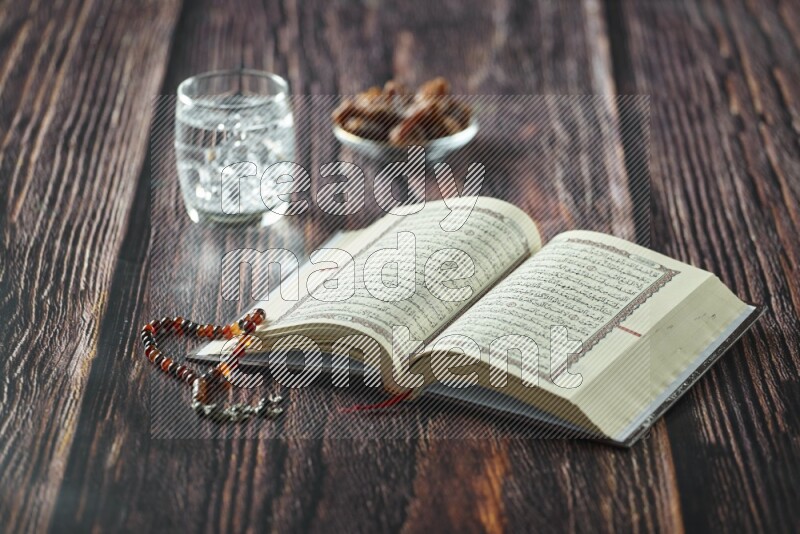 Quran with dates, prayer beads and different drinks all placed on wooden background