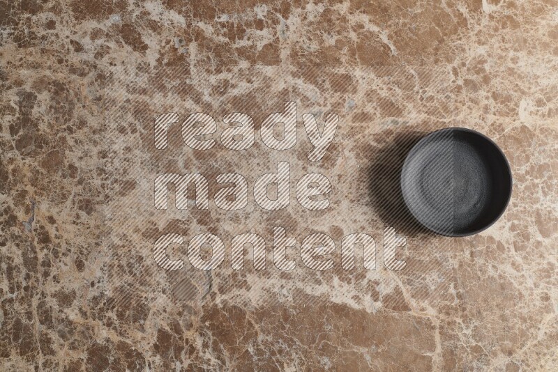 A black pottery bowl on beige marble background