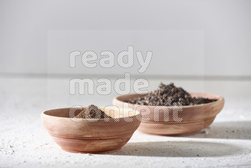 2 wooden bowls full of cloves powder and whole cloves on a textured white flooring