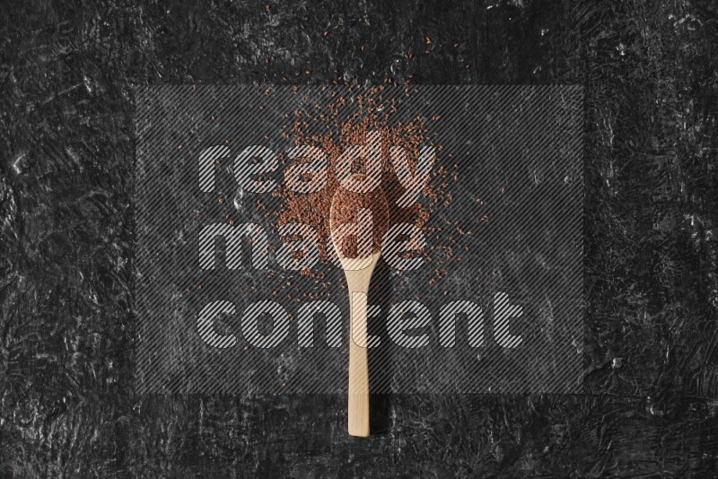 ملعقة خشبية ممتلئة ببذور حب الرشاد محاطه بالبذور علي خلفية سوداء