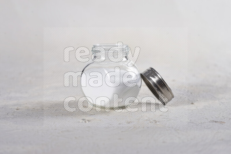 A glass jar full of fine table salt on white background