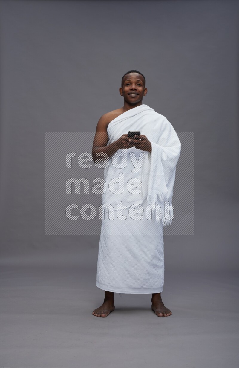 A man wearing Ehram Standing texting on phone on gray background