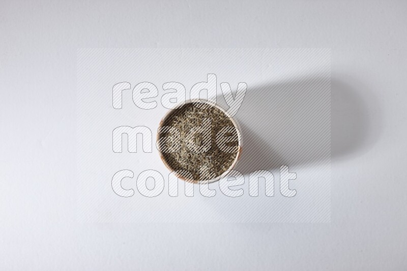 A beige bowl full of cumin seeds on a white flooring