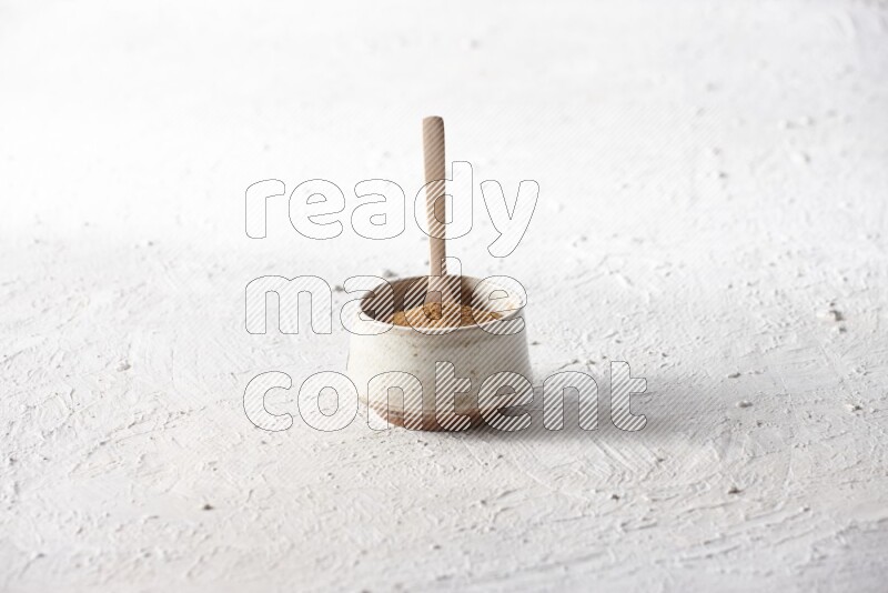 Ceramic beige bowl full of cinnamon powder with a wooden spoon on a textured white background