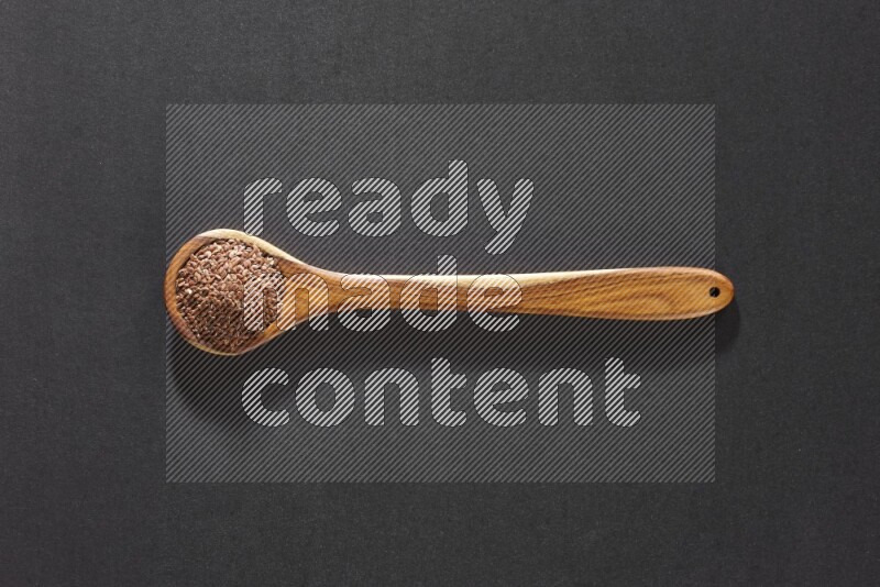 A wooden ladle full of flaxseeds on a black flooring