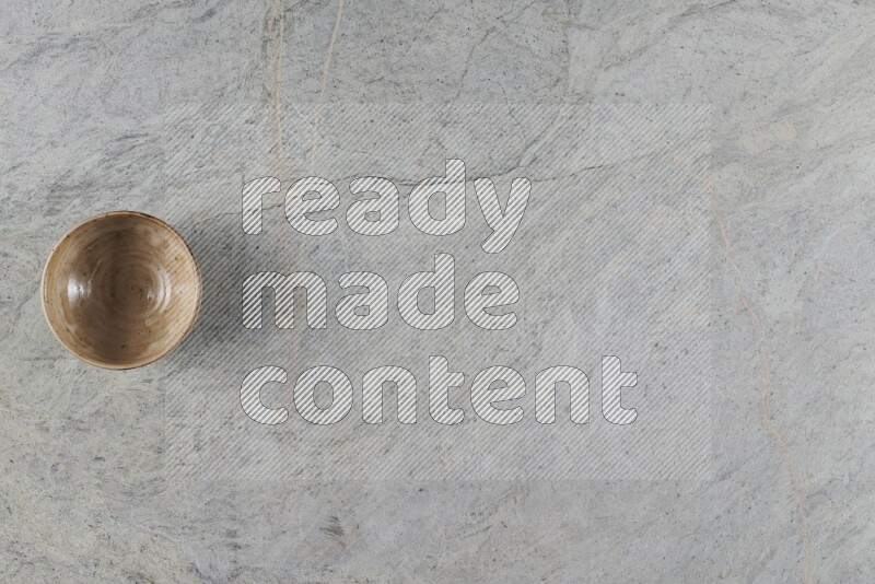 A small beige pottery bowl on grey marble background