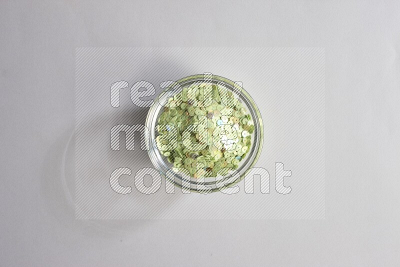 Colored flat sequins in a glass bowl on grey background