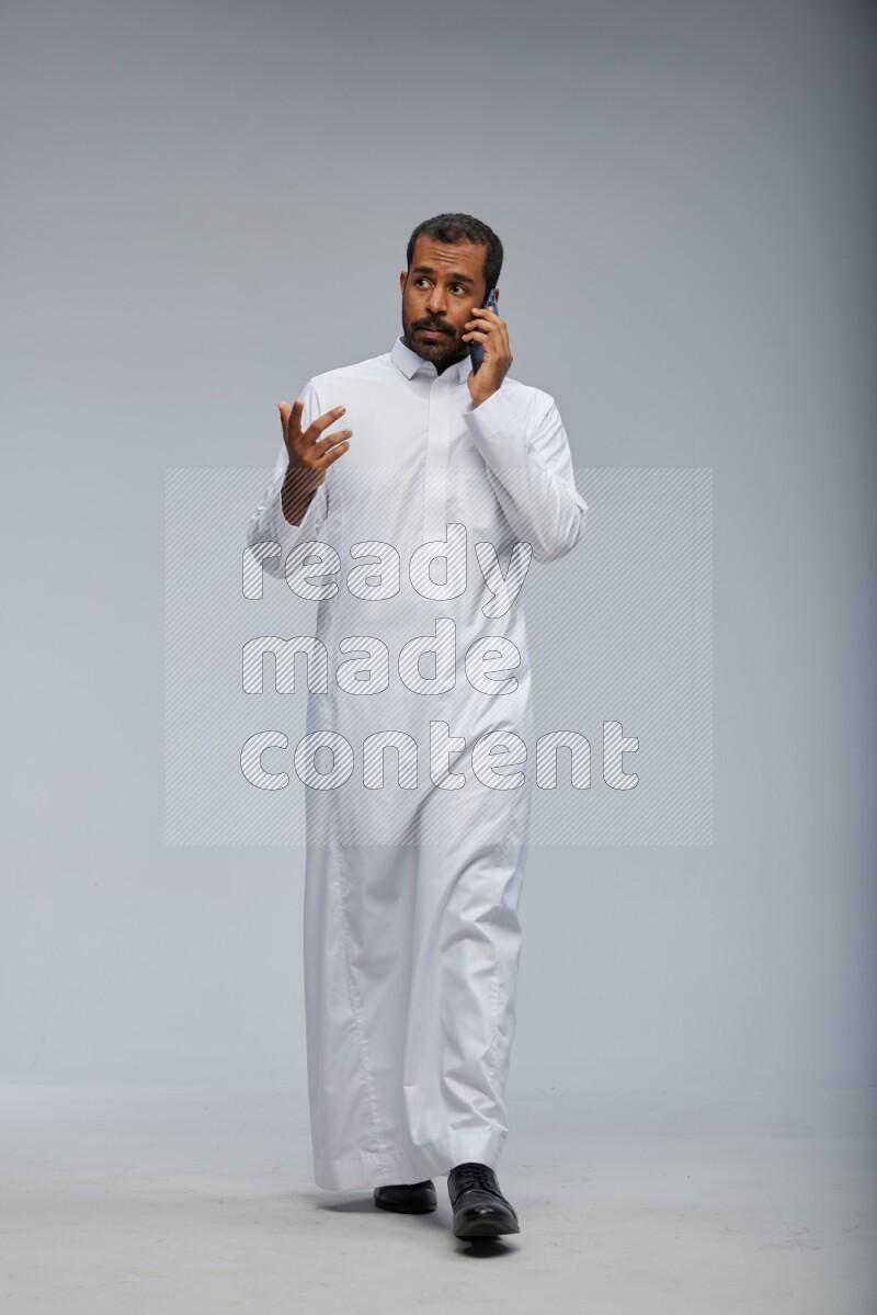 Saudi man wearing Thob standing talking on phone on Gray background