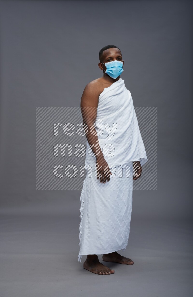 A man wearing Ehram with face mask Standing Interacting with the camera on gray background