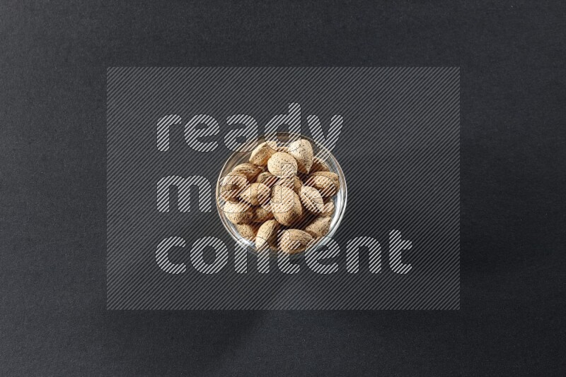 A glass bowl full of almonds on a black background in different angles