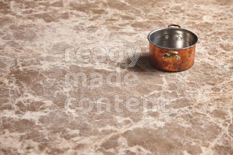 A small copper pot on beige marble background