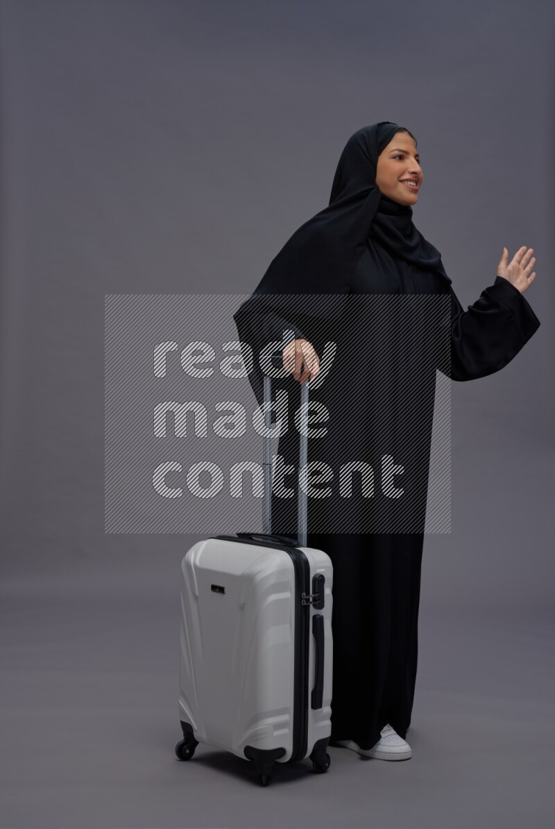 Saudi woman wearing Abaya standing holding bag on gray background