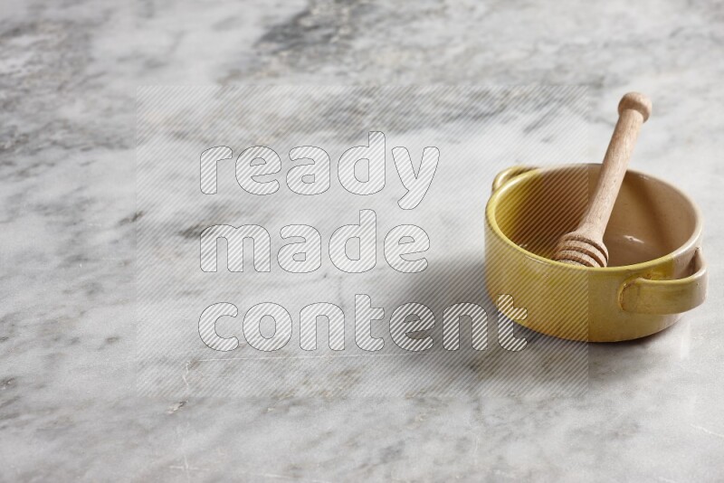 Multicolored pottery bowl with wooden honey dipper in it on grey marble background
