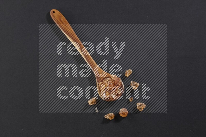 A wooden ladle filled with gum arabic on black flooring