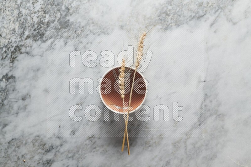 Wheat stalks on brown pottery bowl on grey marble background