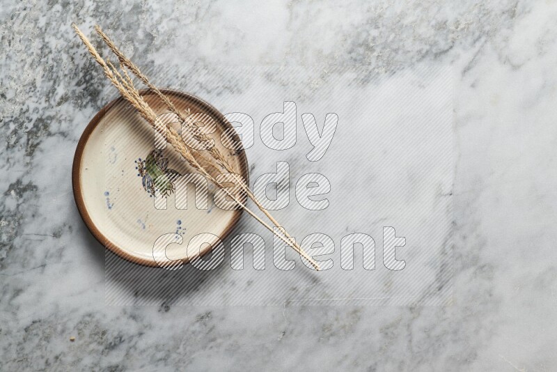 Wheat stalks on decorative pottery plate on grey marble background