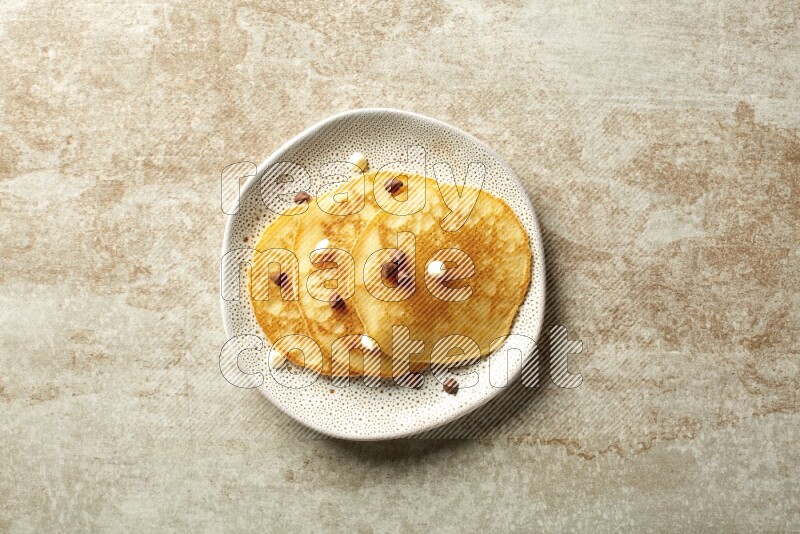 Three stacked chocolate chips pancakes in an irregular plate on beige background