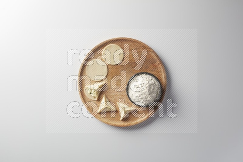 two closed sambosas and one open sambosa filled with cheese while flour aside in a wooden dish on a white background