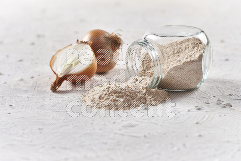 A glass jar full of onion powder flipped with some spilling powder on white background