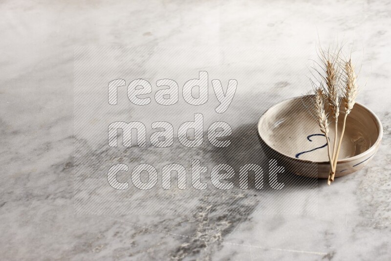Wheat stalks on multicolored pottery bowl on grey marble background