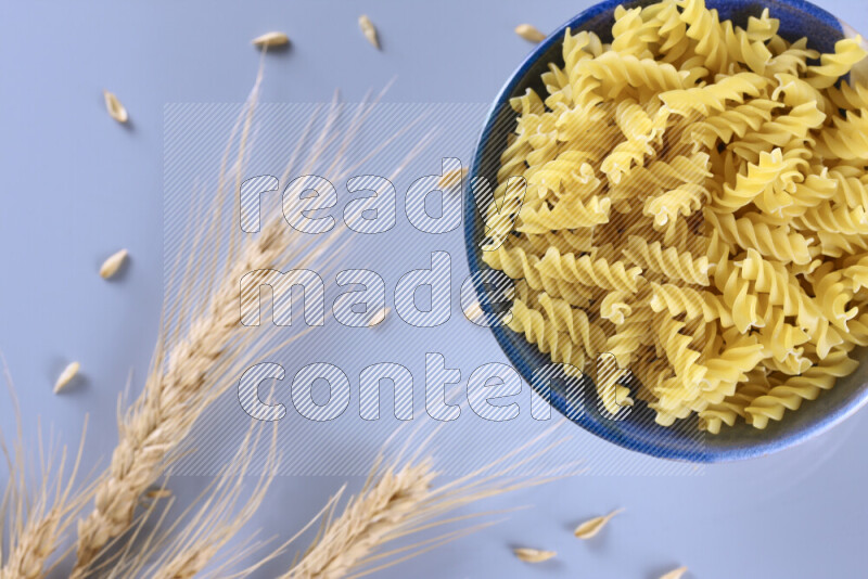 Raw pasta with wheat stalks on light blue background