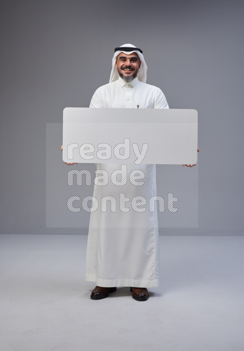 Saudi man Wearing Thob and white Shomag standing holding board on Gray background