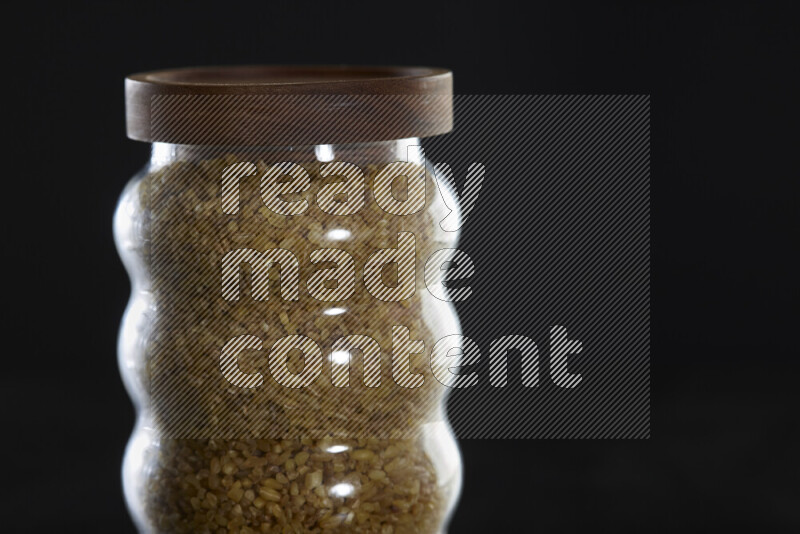 Coarse bulgur in a glass jar on black background