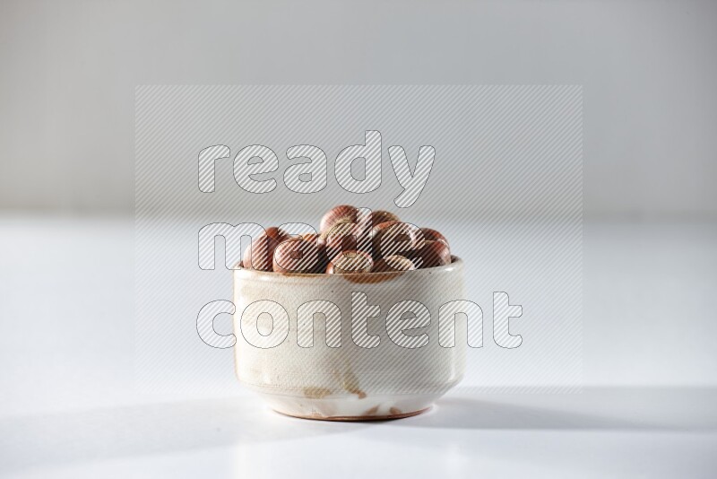 A beige ceramic bowl full of hazelnuts on a white background in different angles