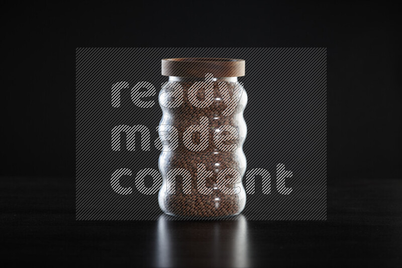 Brown lentils in a glass jar on black background