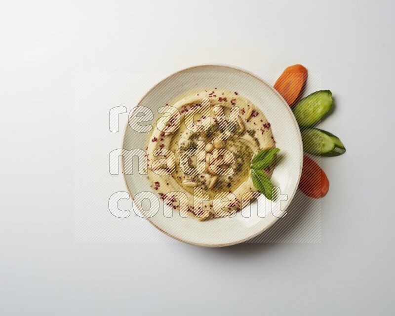 Hummus in a pottry plate garnished with zaatr & sumak on a white background