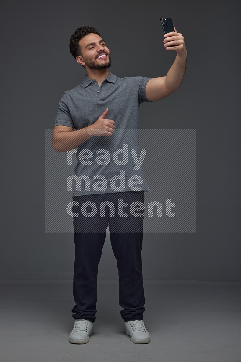 A man wearing casual and taking selfie with his phone different angles eye level on a gray background
