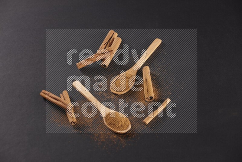 Cinnamon powder in two wooden spoons with cinnamon sticks on black background