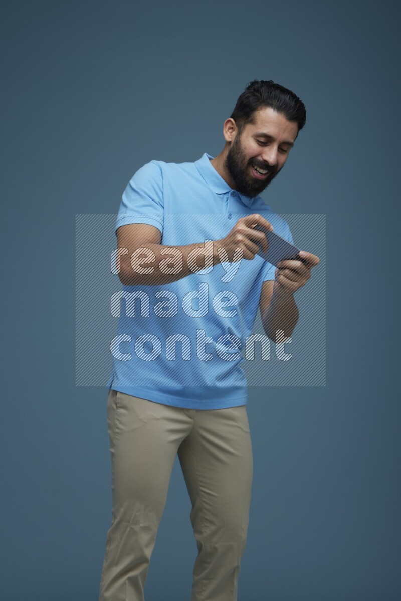 Man playing a game on his phone in a blue background wearing a Blue shirt