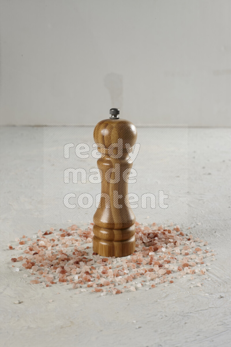 A wooden grinder standing upright and surrounded by coarse pink himalayan salt on white background