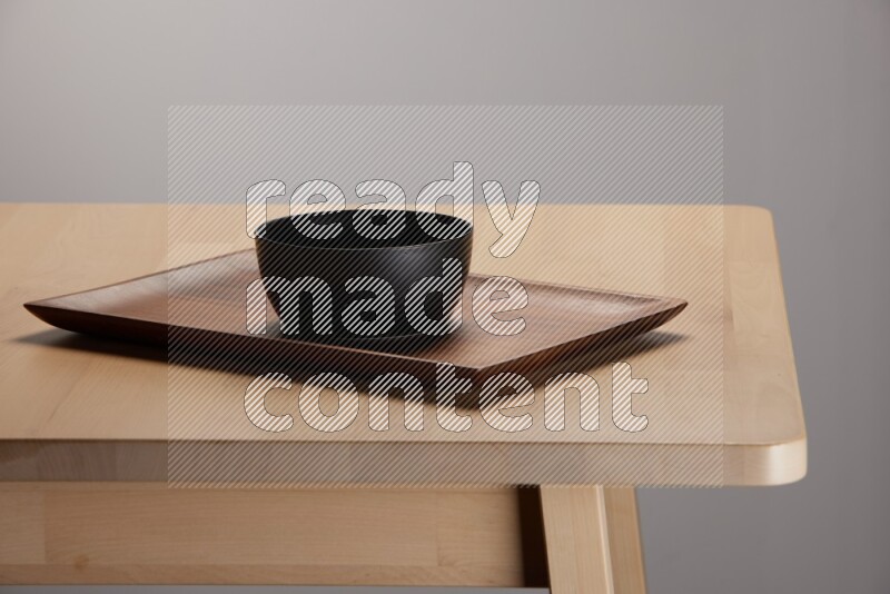 black bowl placed on a rectangular wooden tray on the edge of wooden table