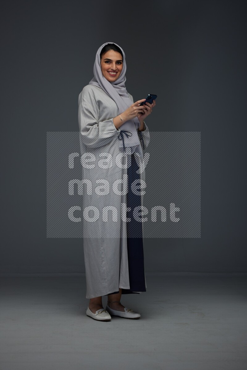 A Saudi woman Texting wearing Grey Abaya on a grey background