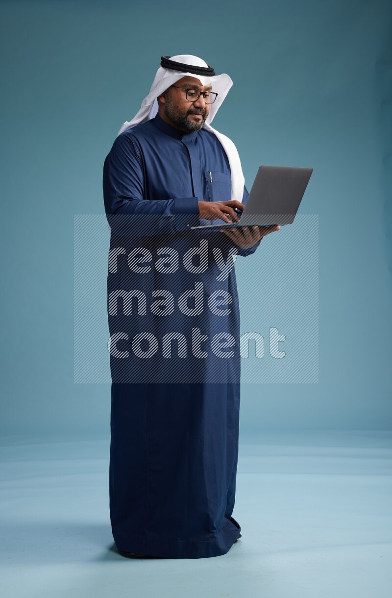 Saudi Man with shimag Standing working on laptop on blue background