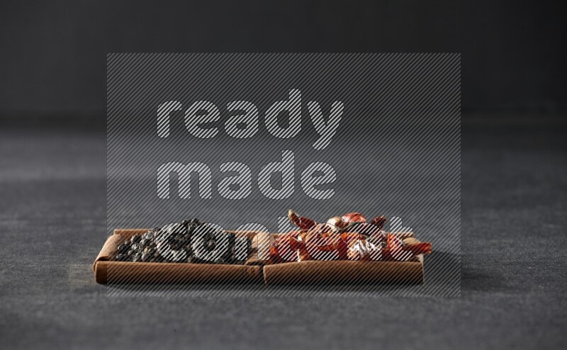 2 squares of cinnamon sticks full of chilis and black peppers on black flooring