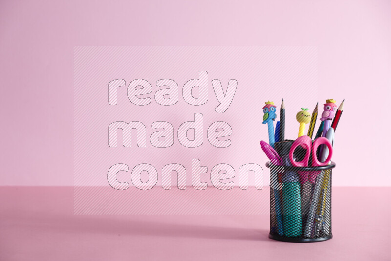 Pens, pencils and other different school supplies in a metal pen holder on rose background