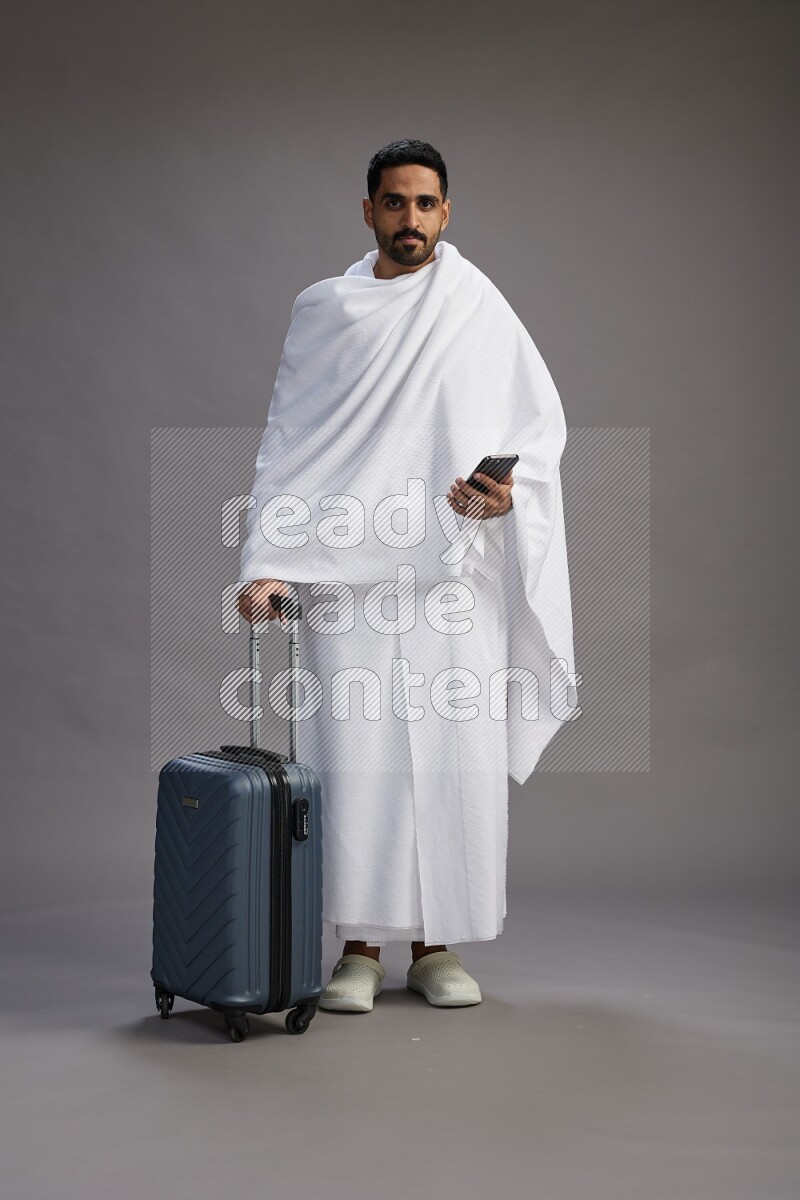 A man wearing Ehram Standing holding traveling bag on gray background