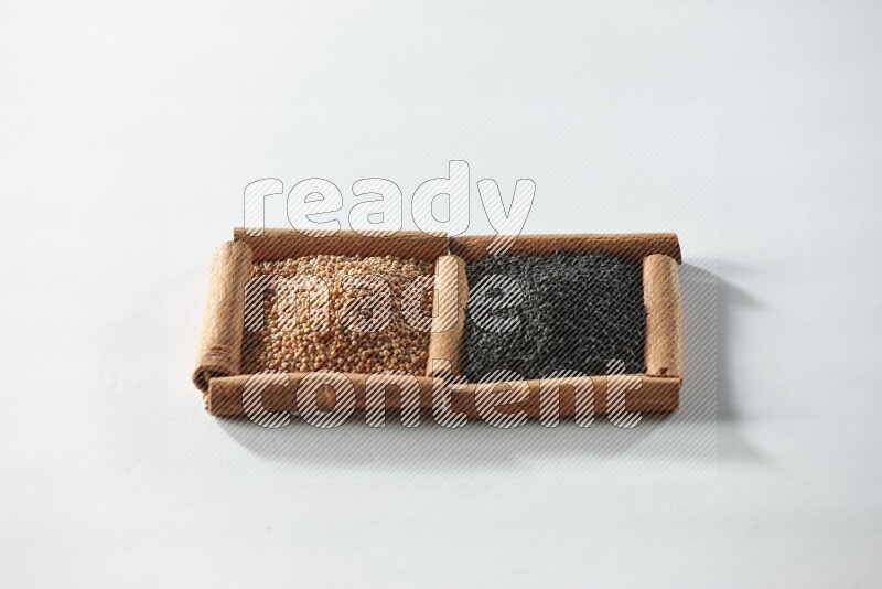 مربعان من أعواد القرفة ممتلئان بحبوب الخردل وحبة البركة السوداء علي خلفية بيضاء