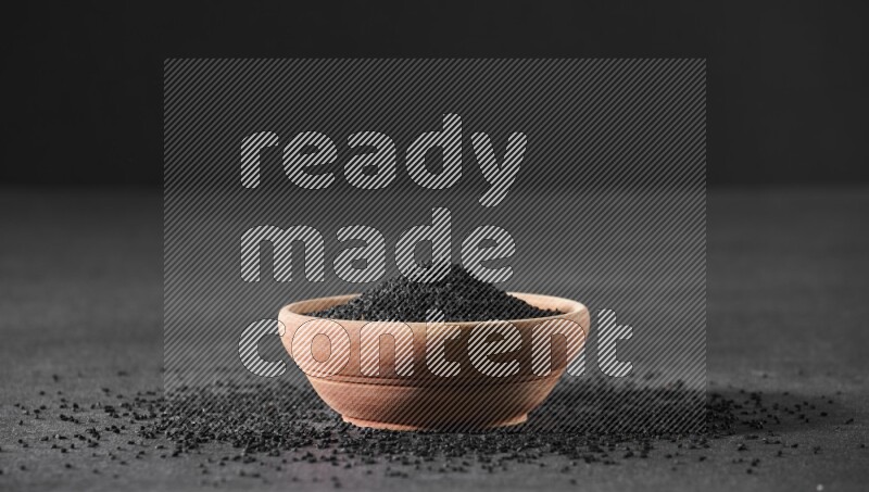 وعاء خشبي ممتلئ ببذور حبة البركة محاط ببعض البذور علي خلفية سوداء