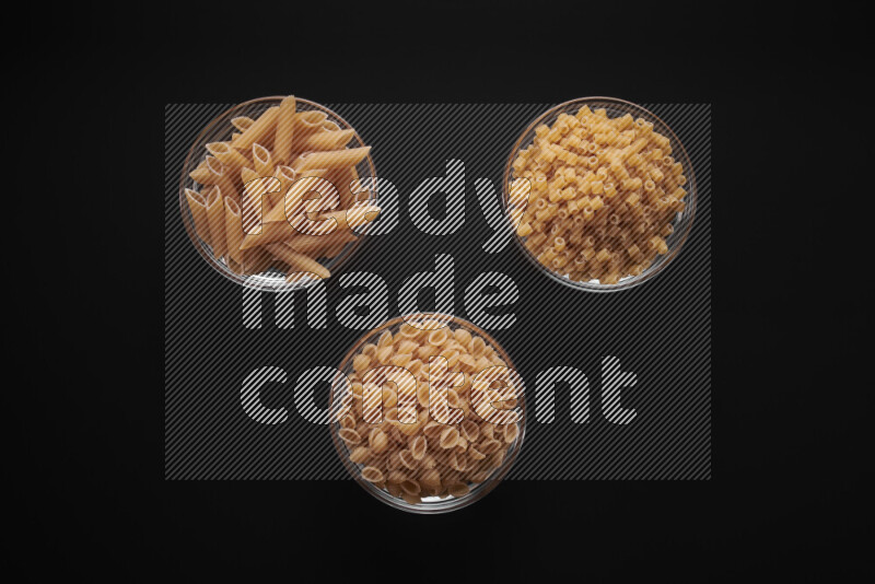 Different pasta types in glass bowls on black background