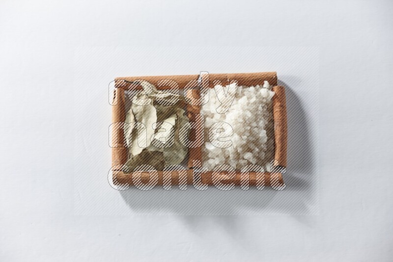 مربعان من أعواد القرفة ممتلئان بالملح الأبيض وأوراق الغار علي خلفية بيضاء