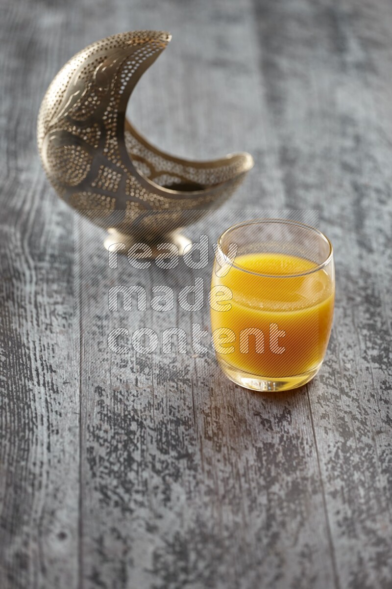 A silver lantern with different drinks, dates, nuts, prayer beads and quran on grey wooden background