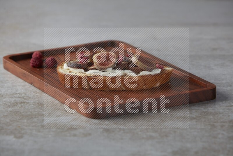 figs slices  with cream cheese on toasted sourdough slice on a wooden board on textured grey background
