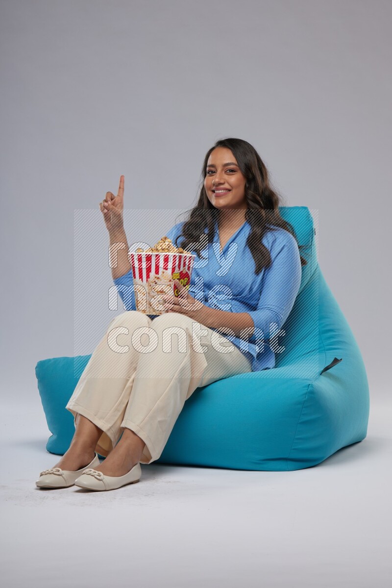 A woman sitting on a blue beanbag and eating popcorn